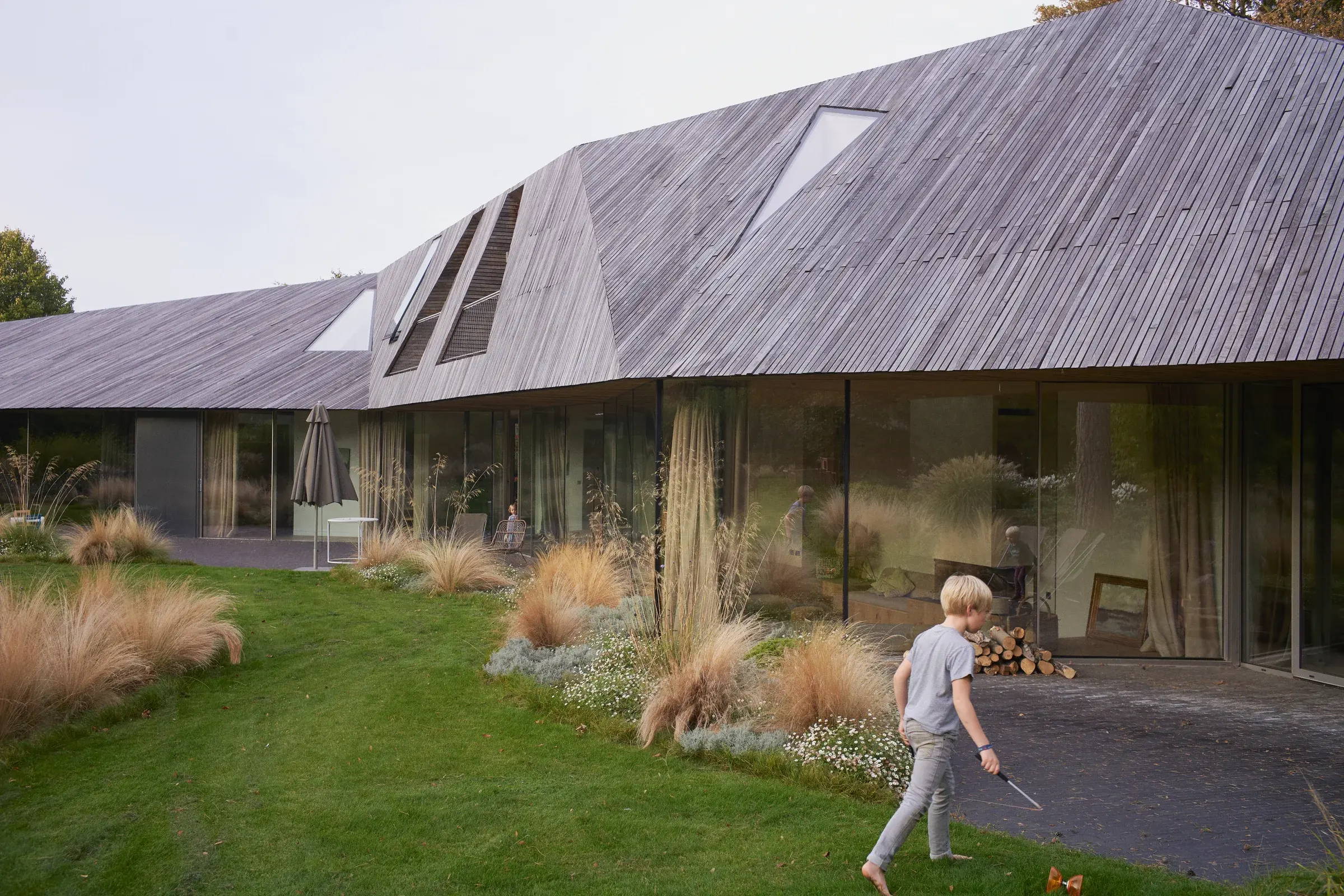 Boomerang House by TANK Architectes in Lille, France, with a folded timber roof above the glazed ground floor, Photography Julien Lanoo